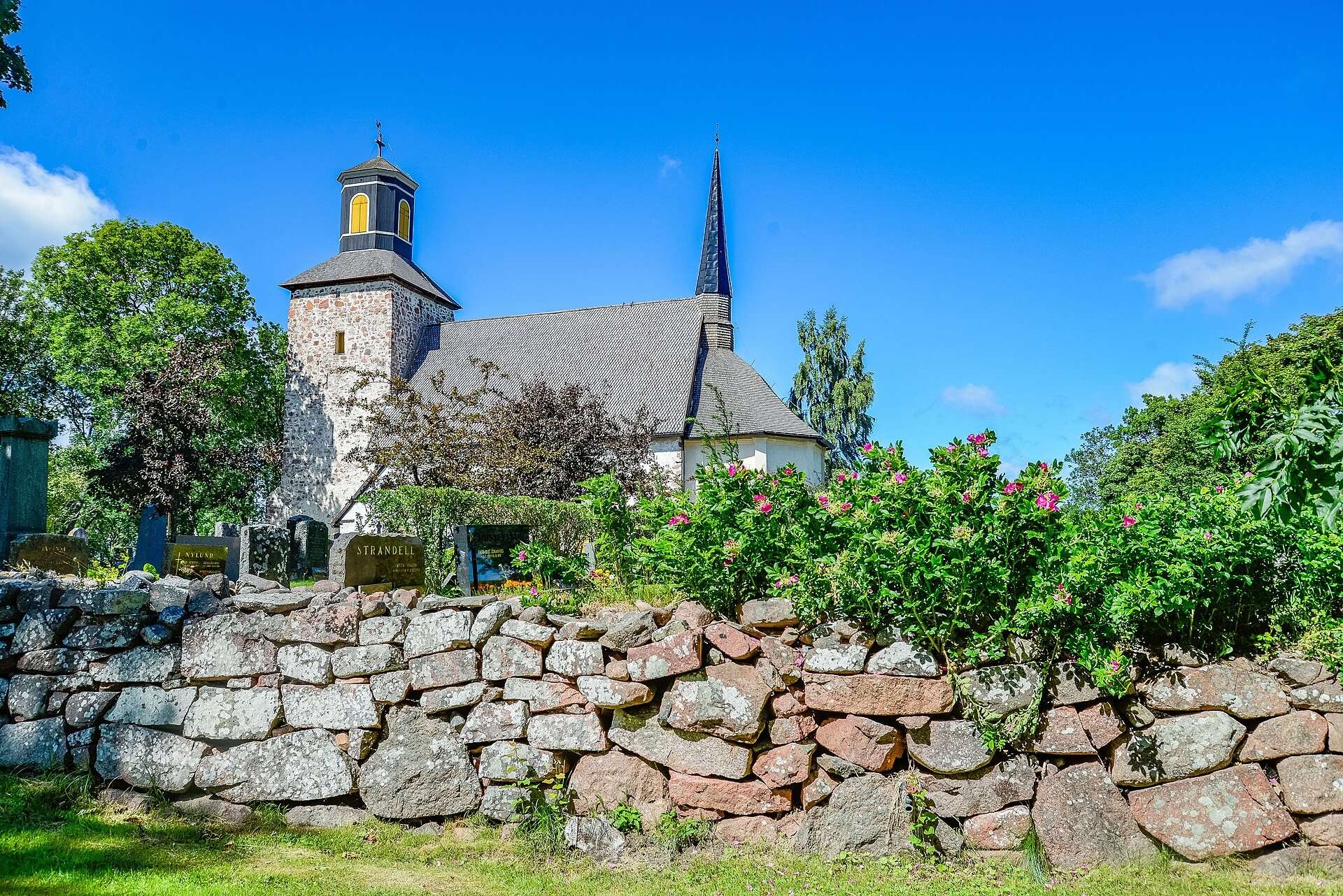 Lemlands kyrka bakom den röda kallmurade stenmuren